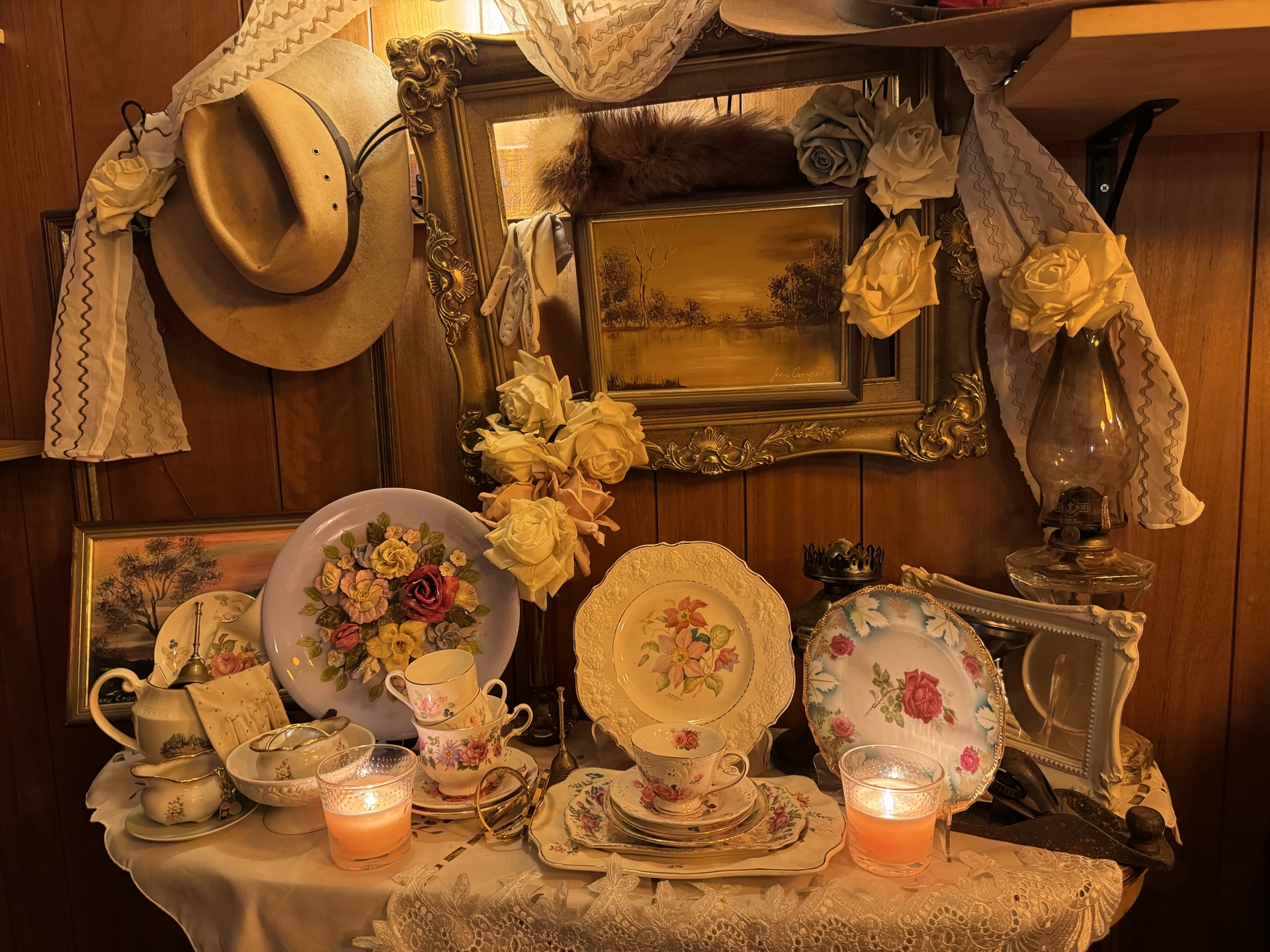 Owner-created Old England tablescape with floral china, lace, framed artwork, gloves, candles and amber lighting